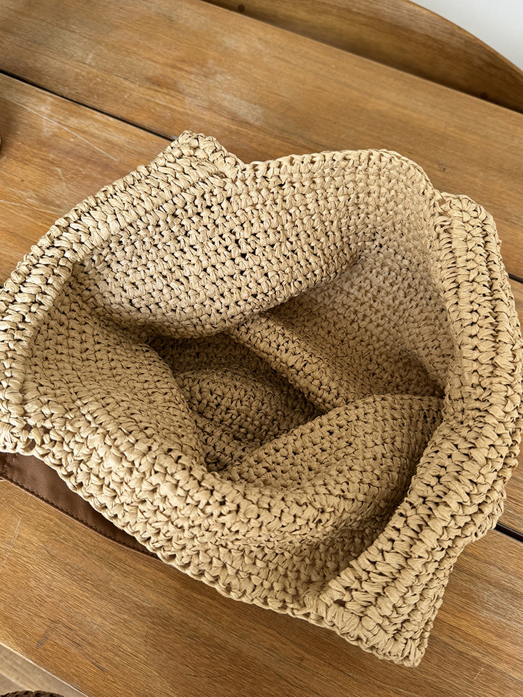 Top view into the bare crochet interior of the straw bag on a wooden table, unlined and open