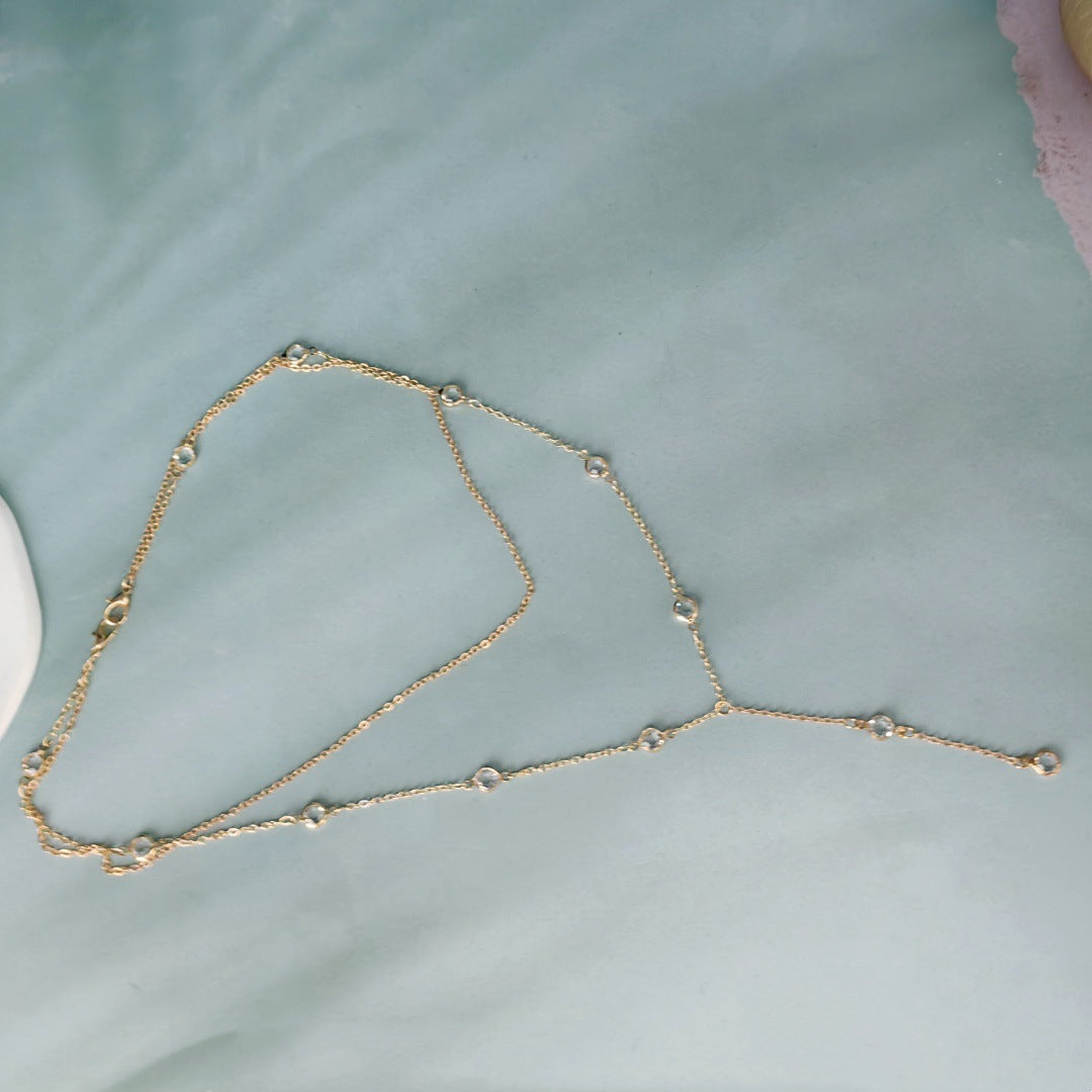 Gold tone layered Y drop rhinestone necklace laid flat on a pale green surface