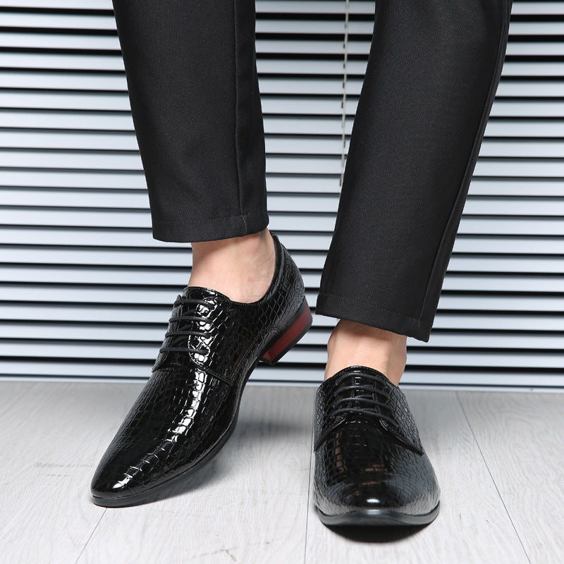 Man wearing black crocodile embossed derby shoes with black suit trousers on a light floor