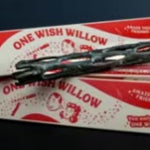 Dark knotted willow style wand laid across its printed red and white retail box