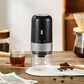 Black electric coffee grinder on a table with coffee beans, a cup of coffee and a pour-over dripper