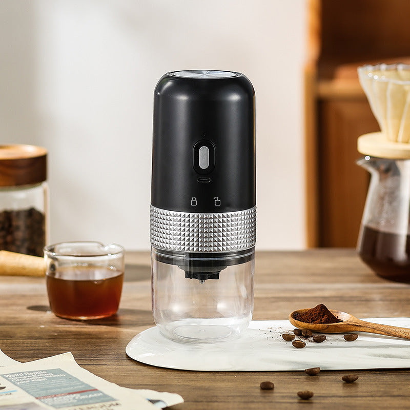 Black electric coffee grinder on a table with coffee beans, a cup of coffee and a pour-over dripper