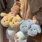 Yellow puppy slippers and blue gray puppy slippers held in two hands against a fleece jacket
