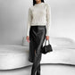 Woman in sunglasses wearing a black PU leather midi skirt, cream sweater and black handbag on a white sofa