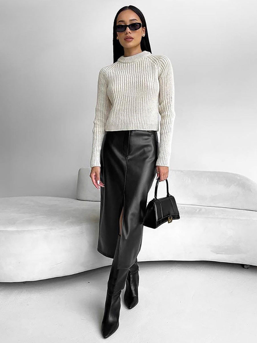 Woman in sunglasses wearing a black PU leather midi skirt, cream sweater and black handbag on a white sofa