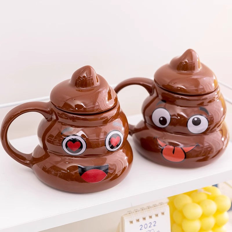 Brown ceramic poop shaped mug with red heart eyes and a tongue beside a lidded emoji mug