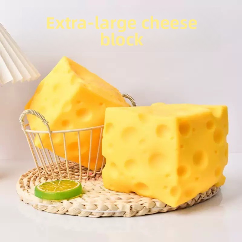 Two large cheese block squishy toys on a woven tray beside a wire basket and a lime slice