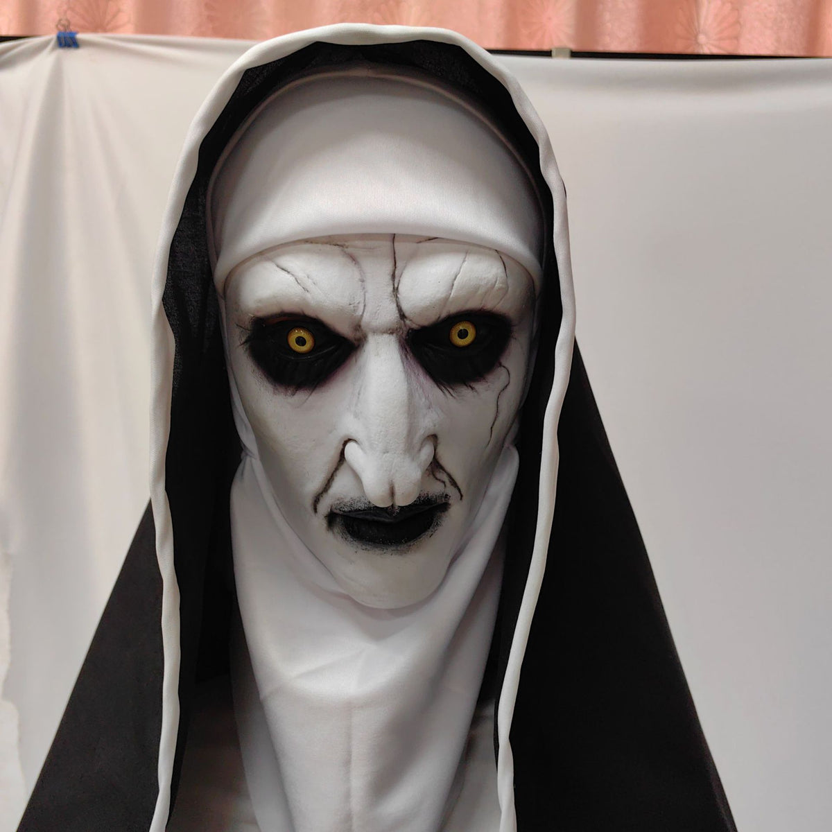 Closed mouth pale nun latex mask with sunken black rimmed eyes and hood