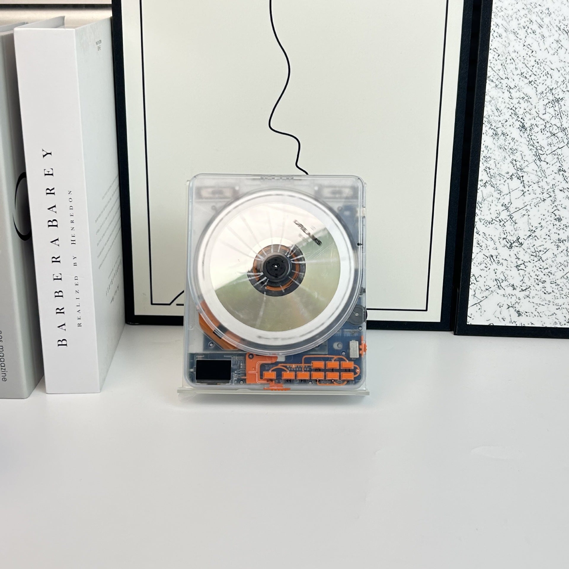 Transparent CD player standing upright on a white desk beside books