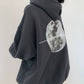 Dark gray oversized hooded sweatshirt seen from behind with a large grayscale moon print and a line of small text