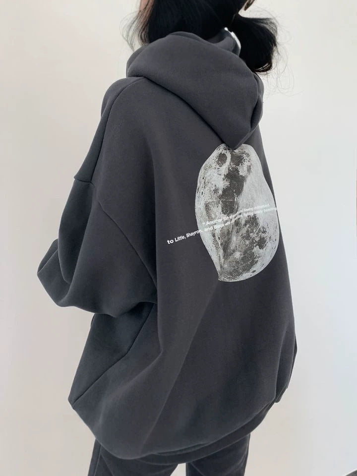 Dark gray oversized hooded sweatshirt seen from behind with a large grayscale moon print and a line of small text