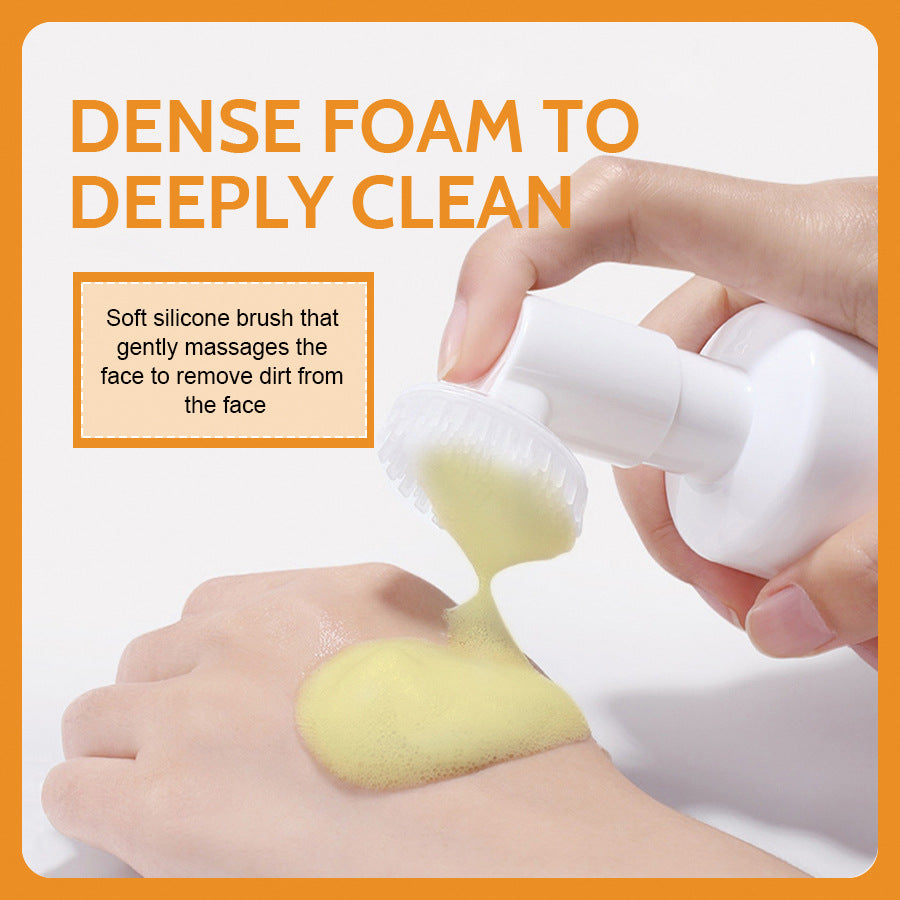 Hand pressing the white pump so pale yellow foam flows through the soft silicone brush dome