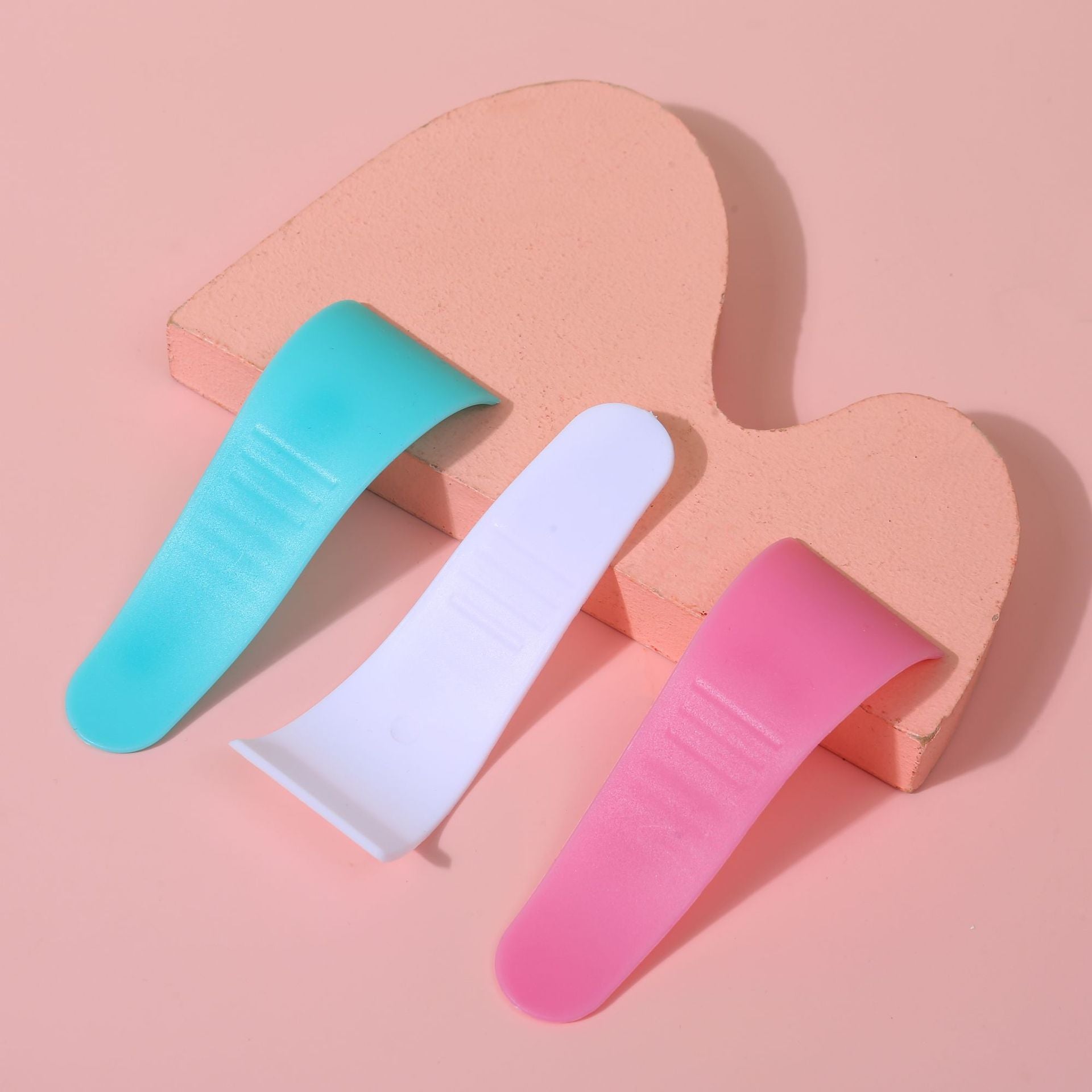 Three hair removal cream scrapers with S curve edge laid flat showing the rounded blade