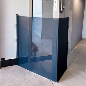 Dark retractable pet gate pulled across a hallway with a cat standing on the far side of the panel