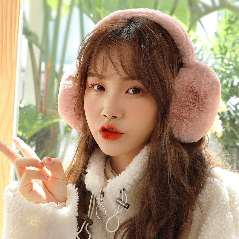 Woman wearing pink plush winter earmuffs with a white teddy fleece jacket