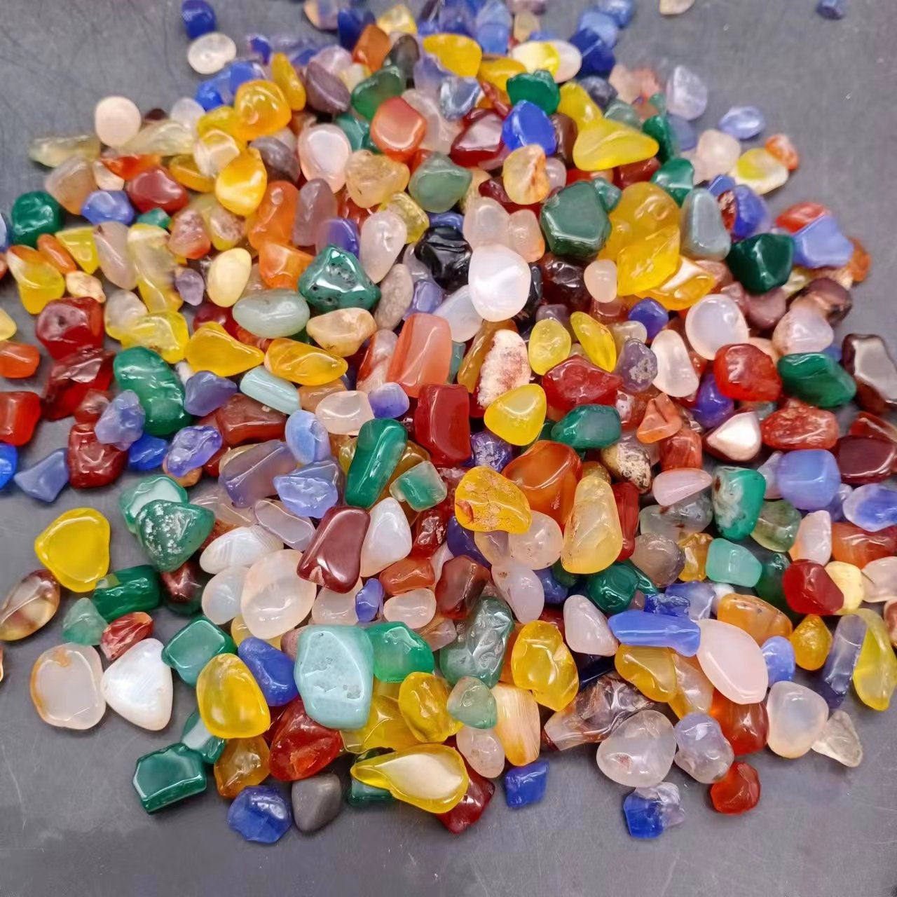 Hand holding a scoop of colourful polished agate pebbles for scale