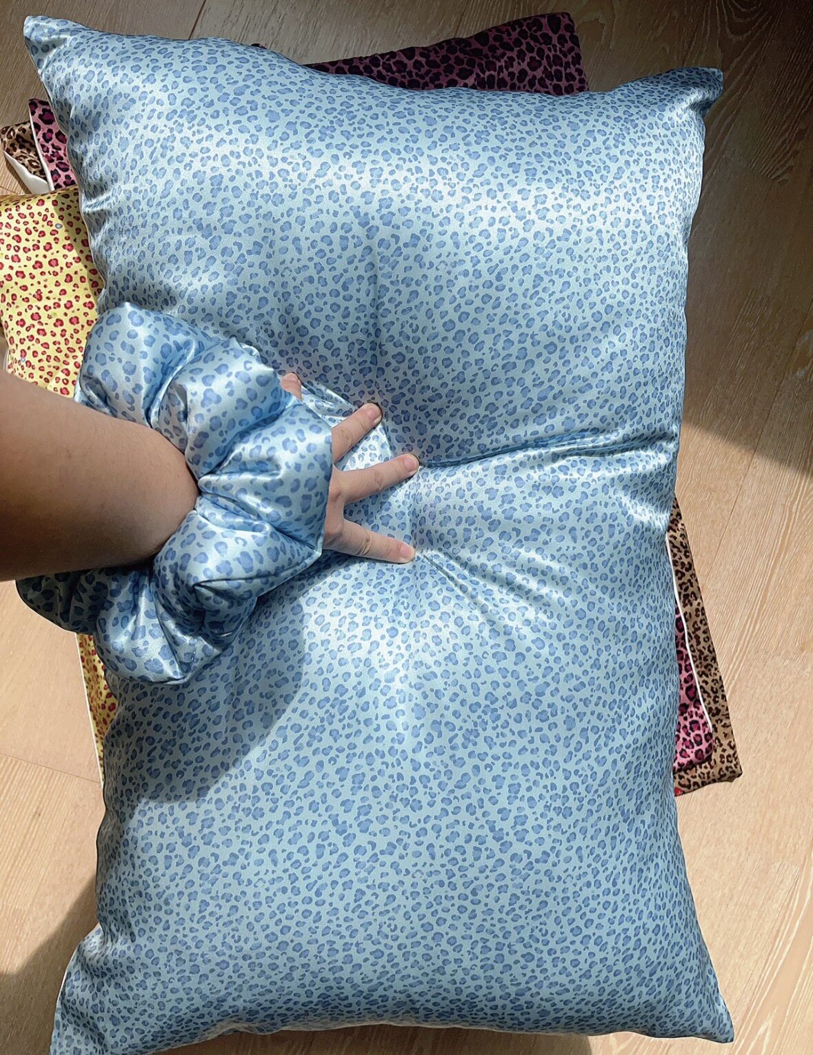 Blue leopard silk pillowcase with a matching scrunchie and a hand on the pillow