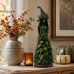 Green variant: witch statue in a green leaf gown beside a vase of autumn leaves and pumpkins