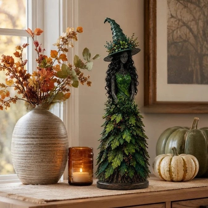 Green variant: witch statue in a green leaf gown beside a vase of autumn leaves and pumpkins