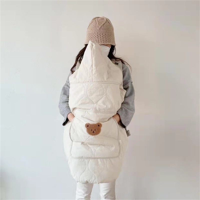 Off-white quilted windproof baby cape worn over a front carrier with bear pocket
