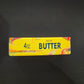 Yellow butter stick squishy toy with a swirled wavy color pattern and a printed butter label, 14 cm