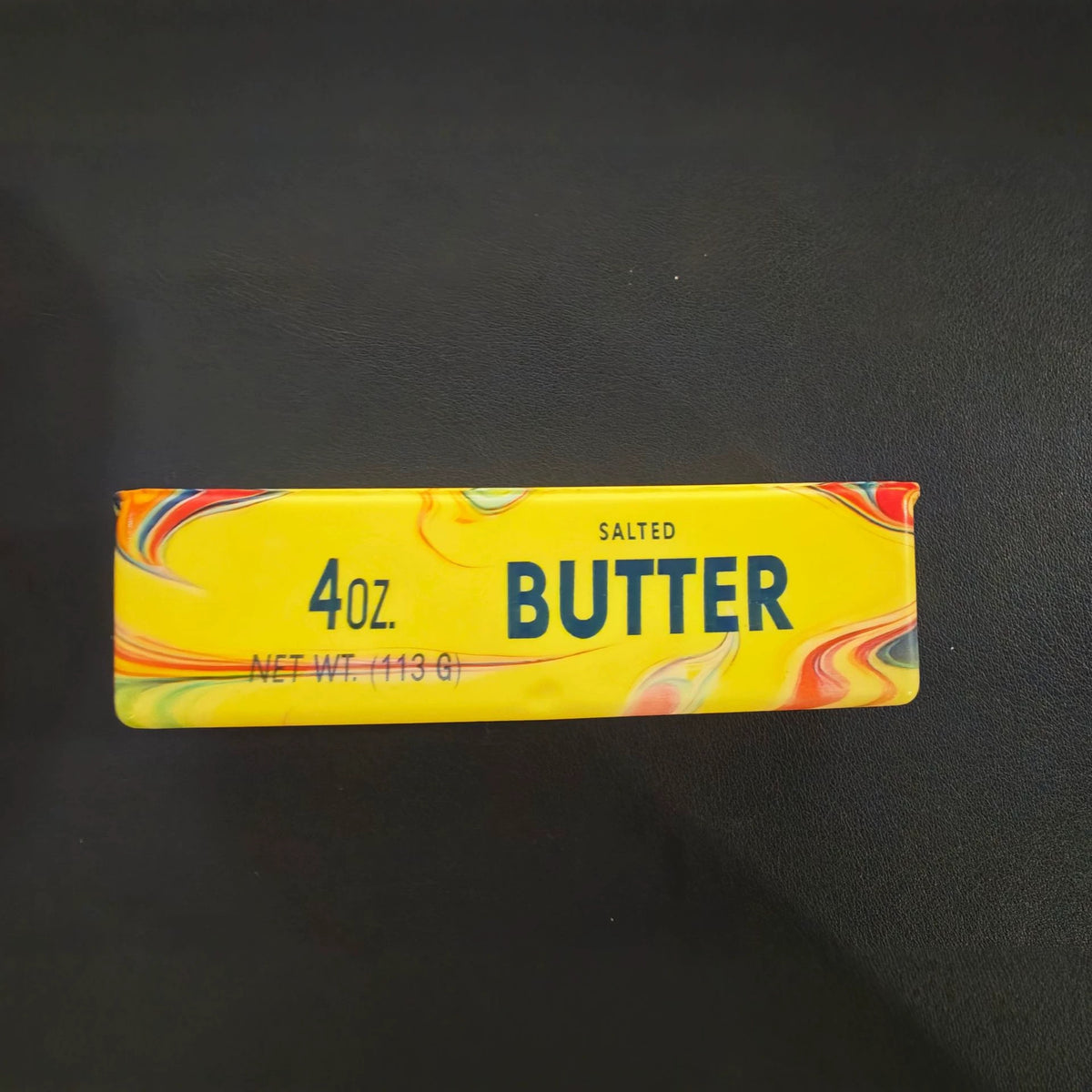 Yellow butter stick squishy toy with a swirled wavy color pattern and a printed butter label, 14 cm