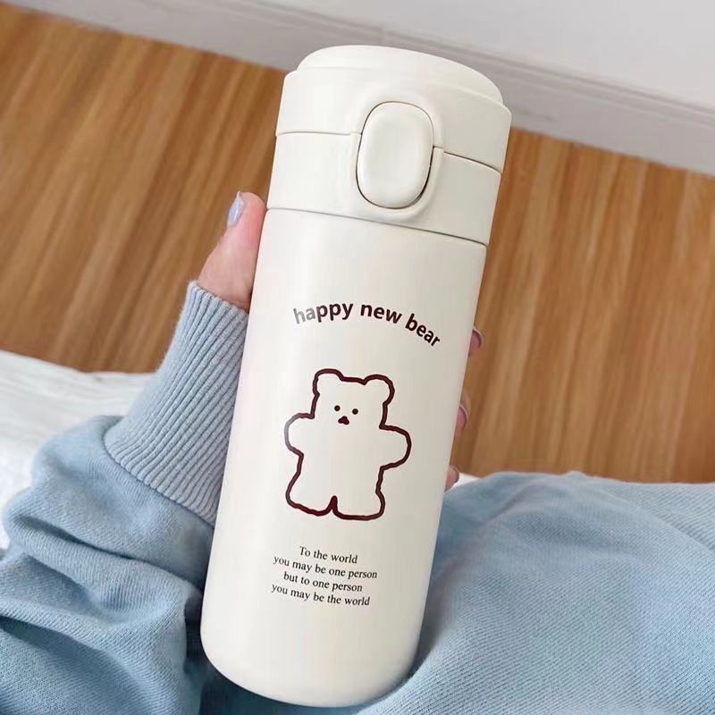 Cream insulated bottle with a brown bear drawing held against a pale blue knitted sleeve