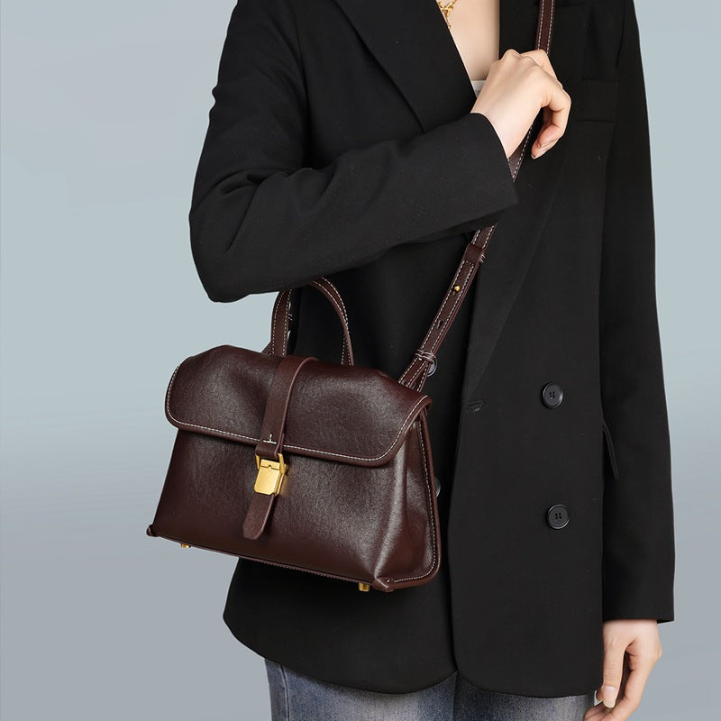 Woman in a black blazer wearing the coffee brown flap satchel across the body with the strap over one shoulder