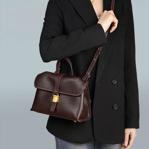 Woman in a black blazer wearing the coffee brown flap satchel across the body with the strap over one shoulder