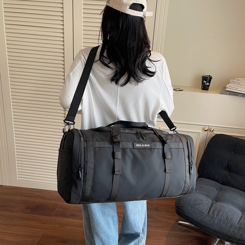 Person carrying a black travel duffel bag over one shoulder by its detachable strap