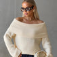 Cream off-shoulder fold-over knit sweater with wide cuffs worn with navy trousers and a clutch