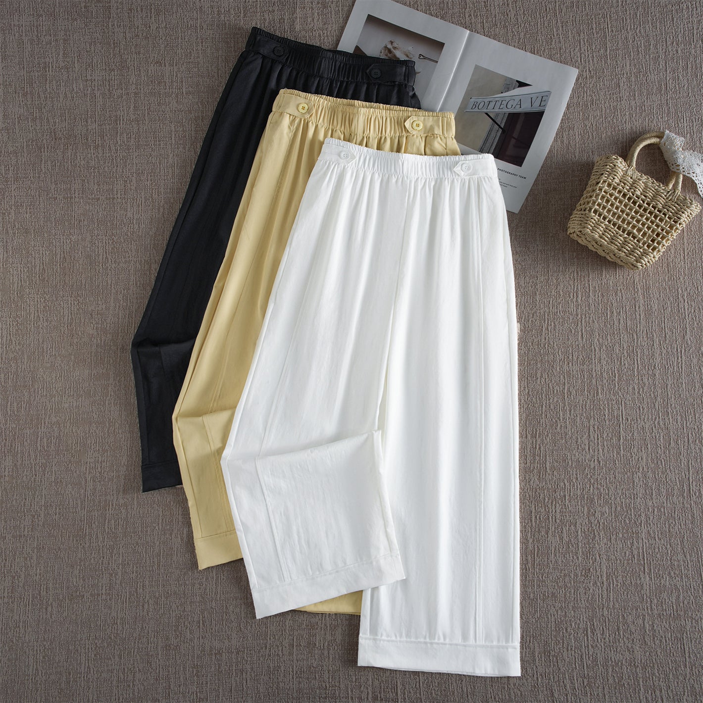 Wide leg high waist pants in white, lemon yellow and black laid flat with a straw bag
