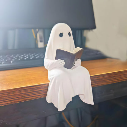 White resin ghost holding an open book, sitting on the edge of a wooden desk beside a keyboard