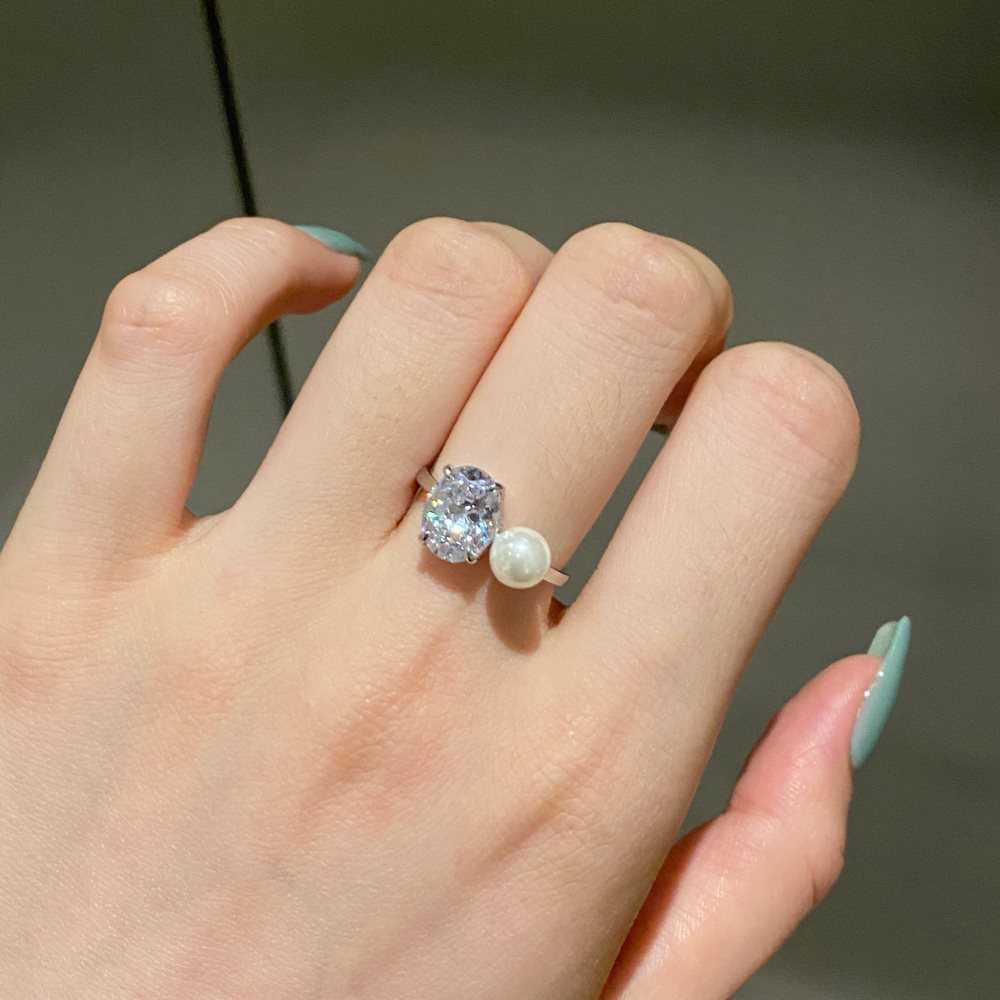 Platinum toned silver ring worn on a finger, clear oval stone and small white imitation pearl