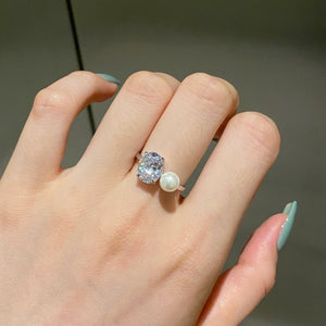 Platinum toned silver ring worn on a finger, clear oval stone and small white imitation pearl