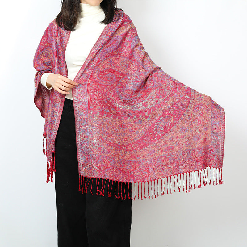 Woman holding out one end of a red paisley shawl showing the large paisley motif, border and red tassels