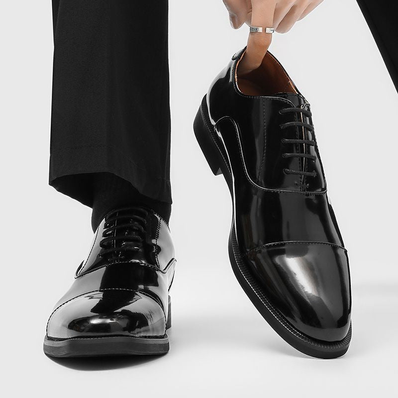 Man in black dress trousers wearing glossy black patent cap toe oxford shoes, lifting one by hand
