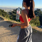 Woman in gray striped pants and a red top seen from behind on a hillside, holding a water bottle