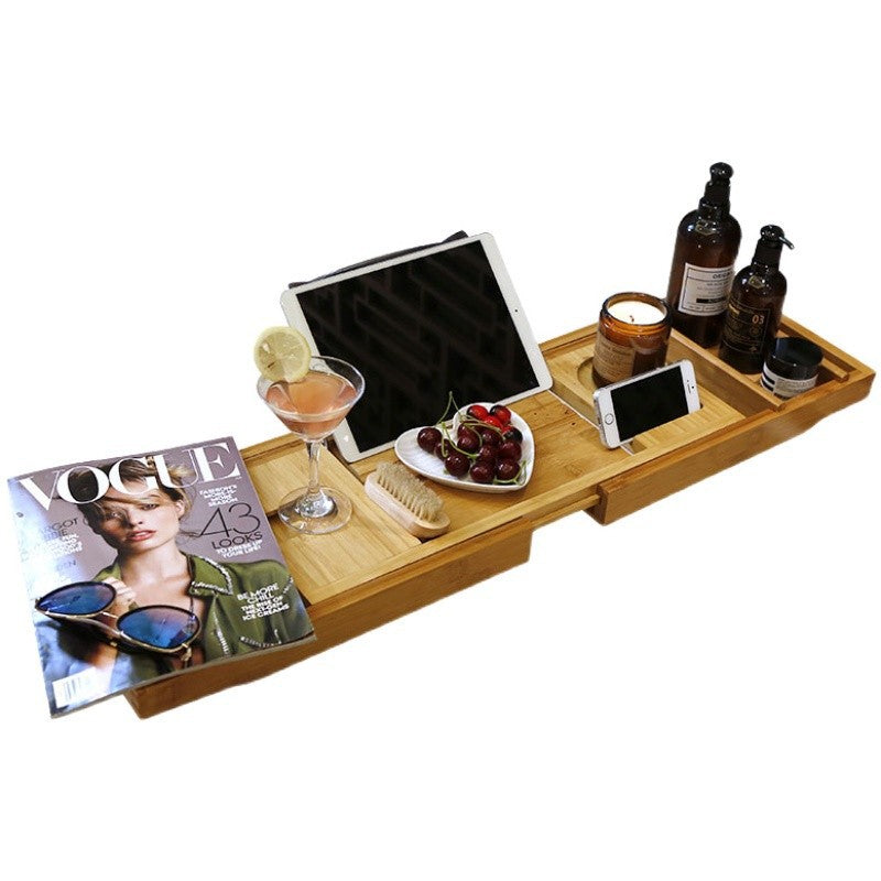 Natural bamboo bathtub caddy tray on a white background with a tablet, a drink, fruit, bottles and a magazine