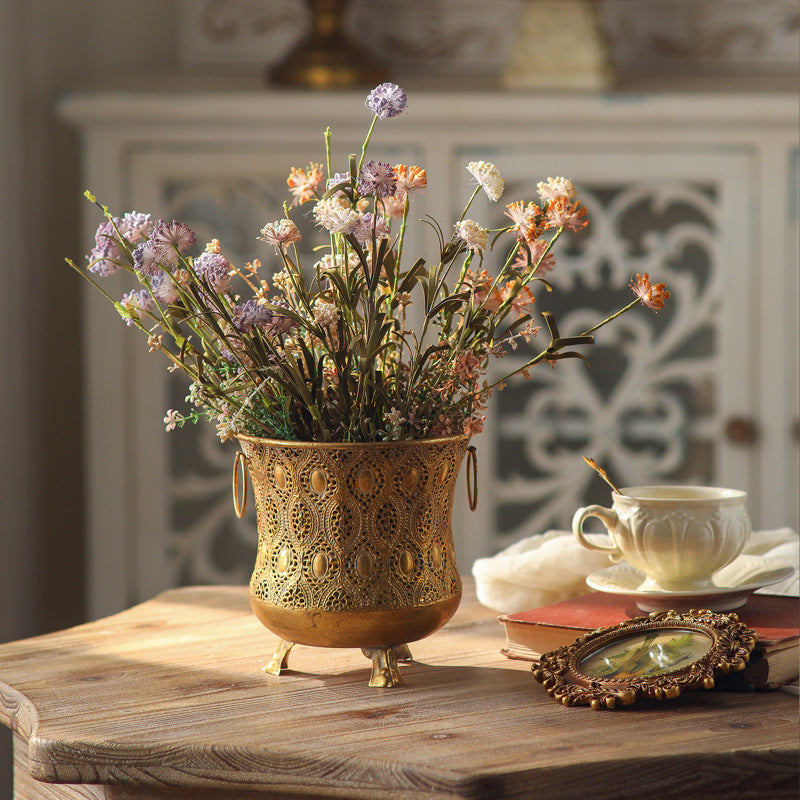 Vintage gold pierced iron flowerpot with two ring handles and wildflowers in a bright room setting