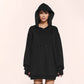 Woman in a black oversized hoodie with the hood up, front pouch pocket and fingerless cuffs on a pale pink background