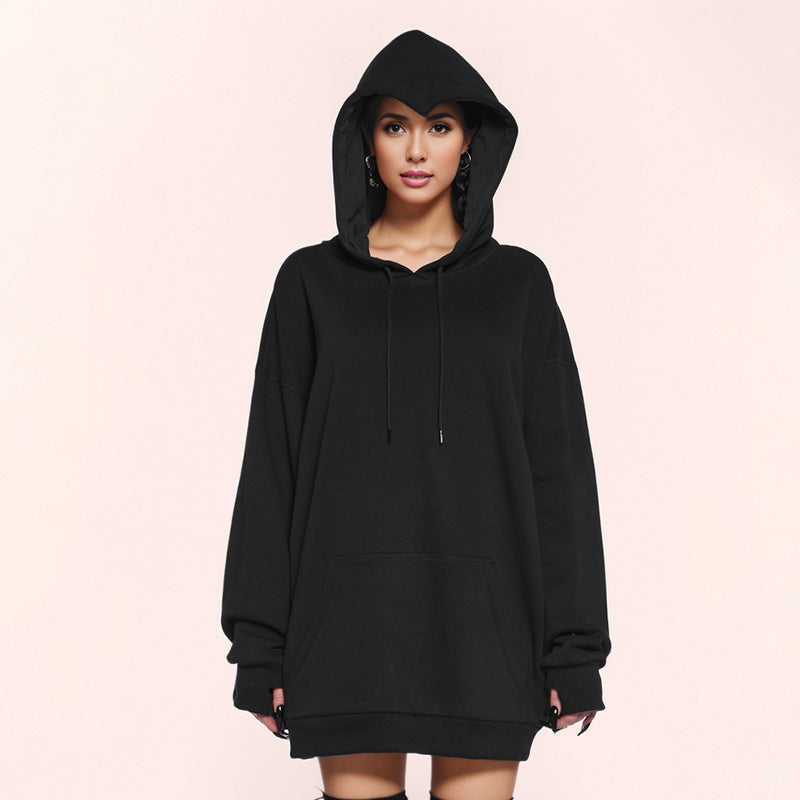 Woman in a black oversized hoodie with the hood up, front pouch pocket and fingerless cuffs on a pale pink background
