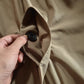 Hand holding a round black button on the khaki coat front placket beside the lapel collar