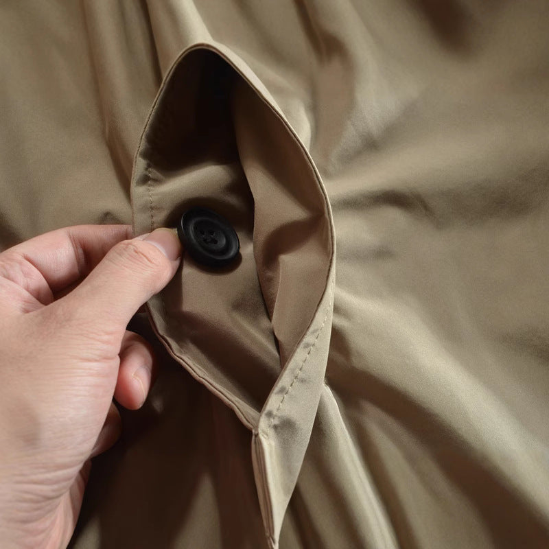 Hand holding a round black button on the khaki coat front placket beside the lapel collar