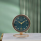 Emerald green dial desk clock with black bezel and gold hands on a round gold tone ring base, green curtain background
