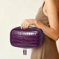 Woman carrying a purple crocodile pattern leather cosmetic bag with double zipper tabs hanging below