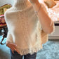 Woman taking a mirror selfie in a cream fringed knit top with an openwork panel and a ribbed collar