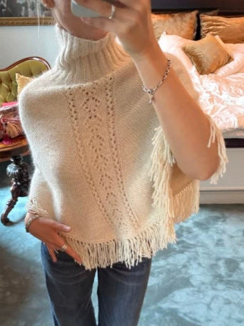 Woman taking a mirror selfie in a cream fringed knit top with an openwork panel and a ribbed collar