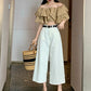 Model in off-white high-waisted wide-leg jeans holding a woven straw bag