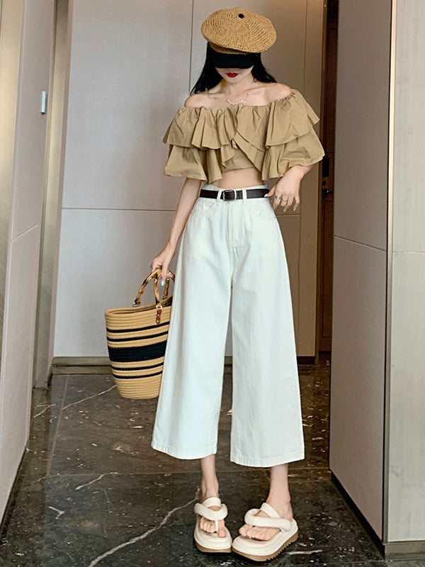 Model in off-white high-waisted wide-leg jeans holding a woven straw bag